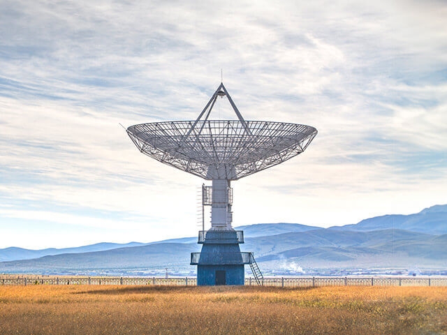 large satellite dish in field with mountains in the background