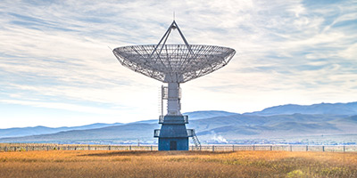 large satellite dish in field with mountains in the background